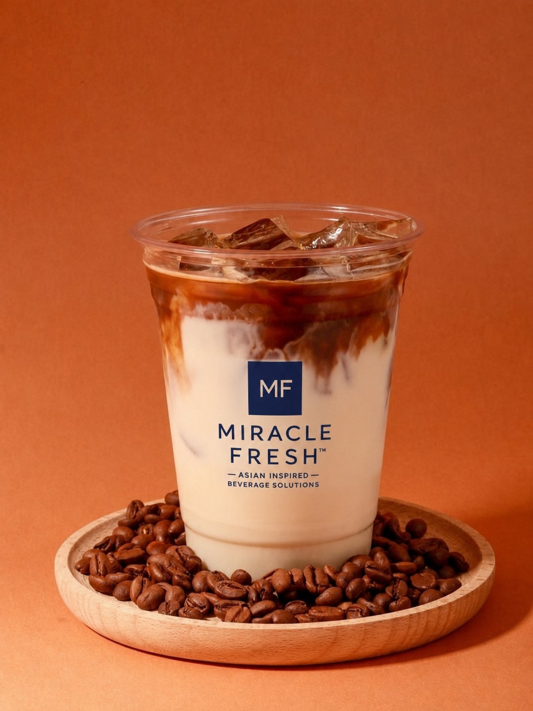 Layered iced coffee with rye milk in a Miracle Fresh cup surrounded by coffee beans