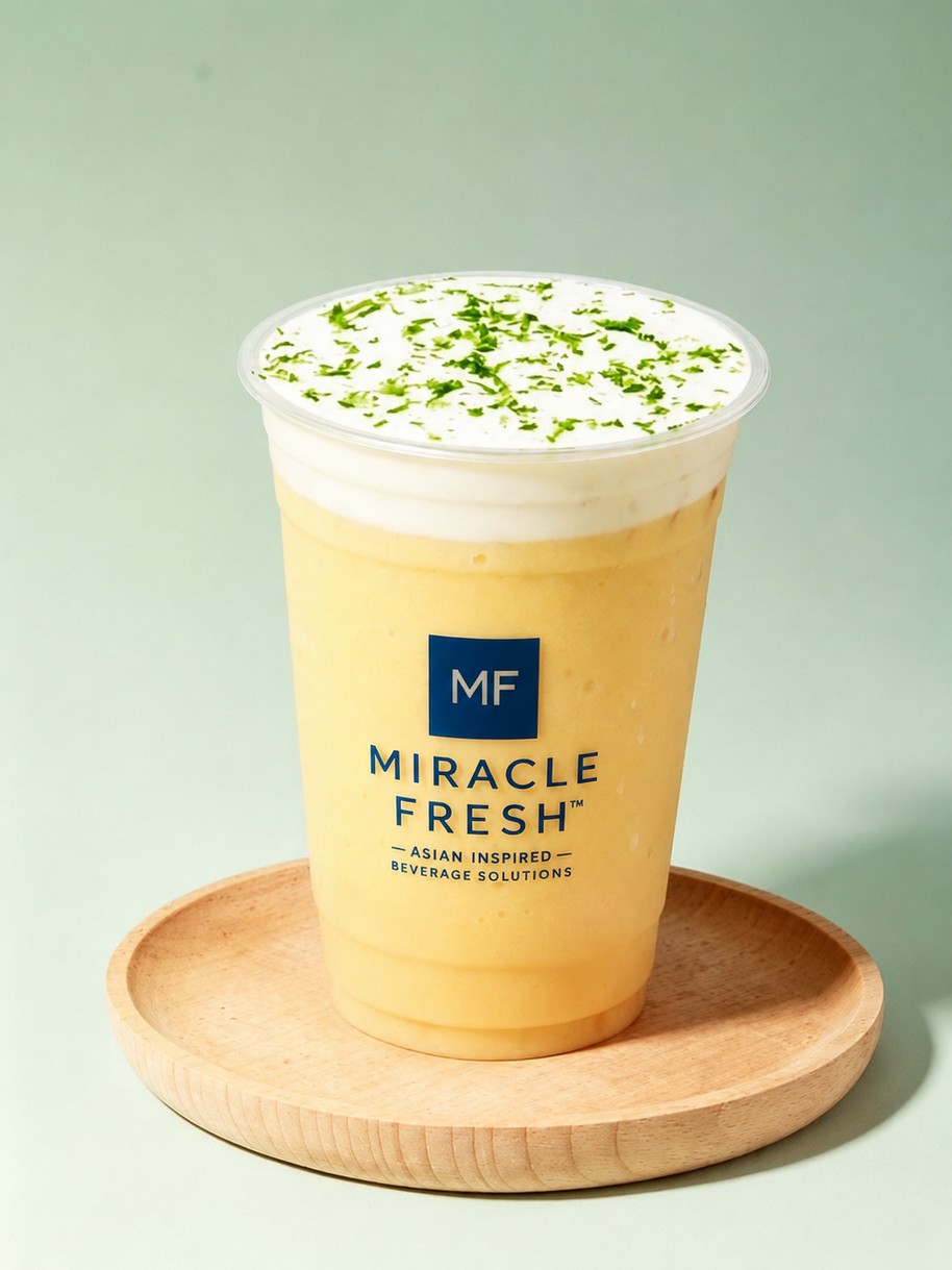 Yellow mango coconut drink topped with white foam and lime zest in a Miracle Fresh cup