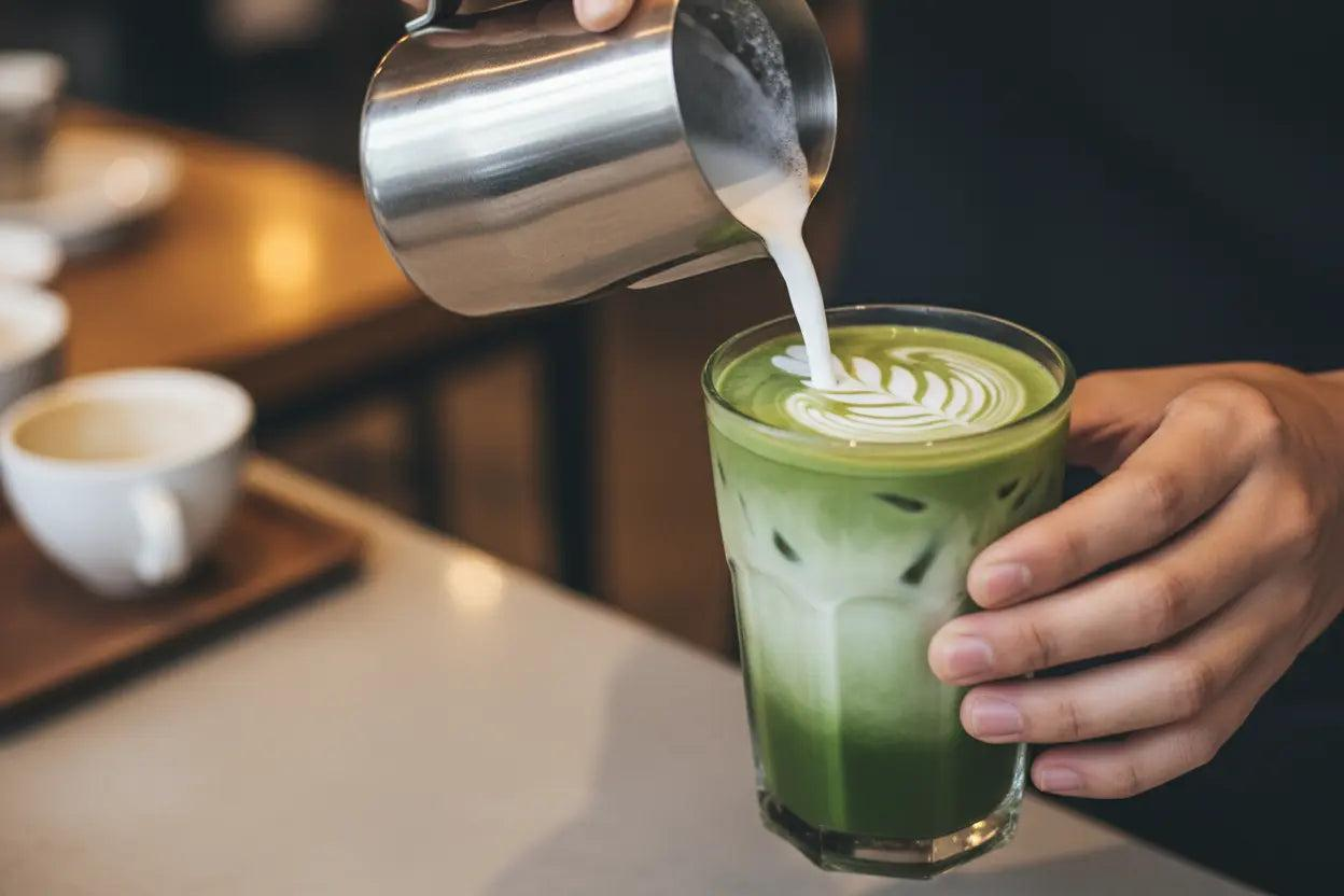 Barista pouring milk into an iced matcha latte with latte art
